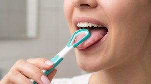 Eine Frau benutzt einen Zungenreiniger bei ihrer täglichen Mundhygiene.